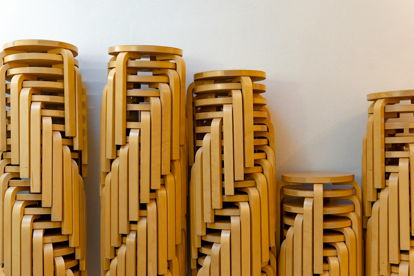 Stacks of wooden stools are leaning against a wall.