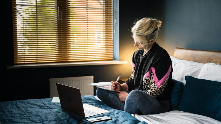 woman in purple and white floral long sleeve shirt and gray pants sitting on bed